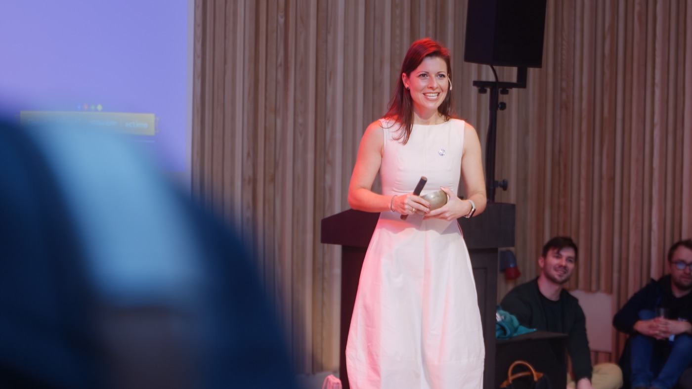 Irma on stage mid-talk, smiling with the audience around her