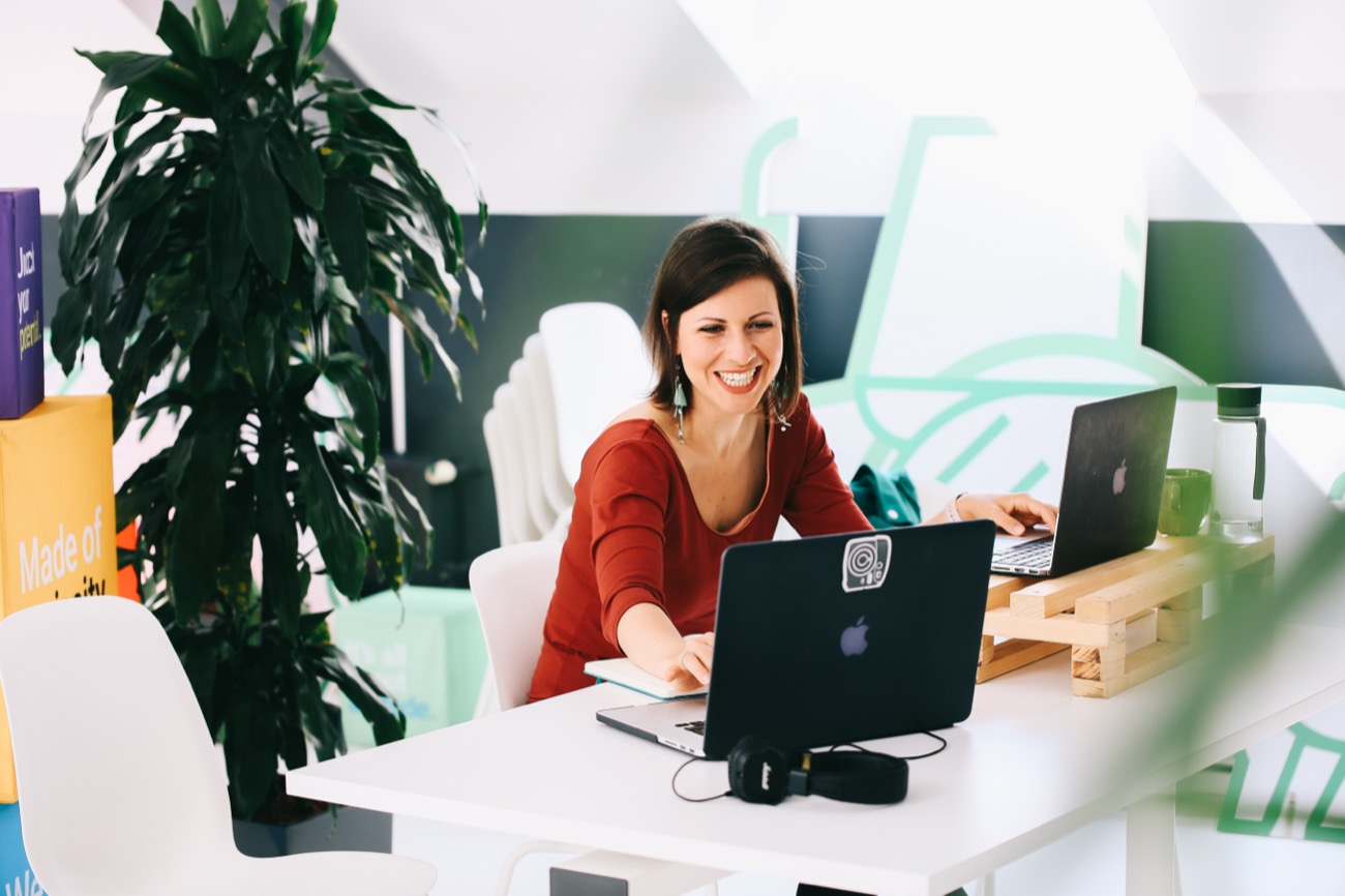 Irma smiling while working at a laptop in a bright, plant-filled workspace