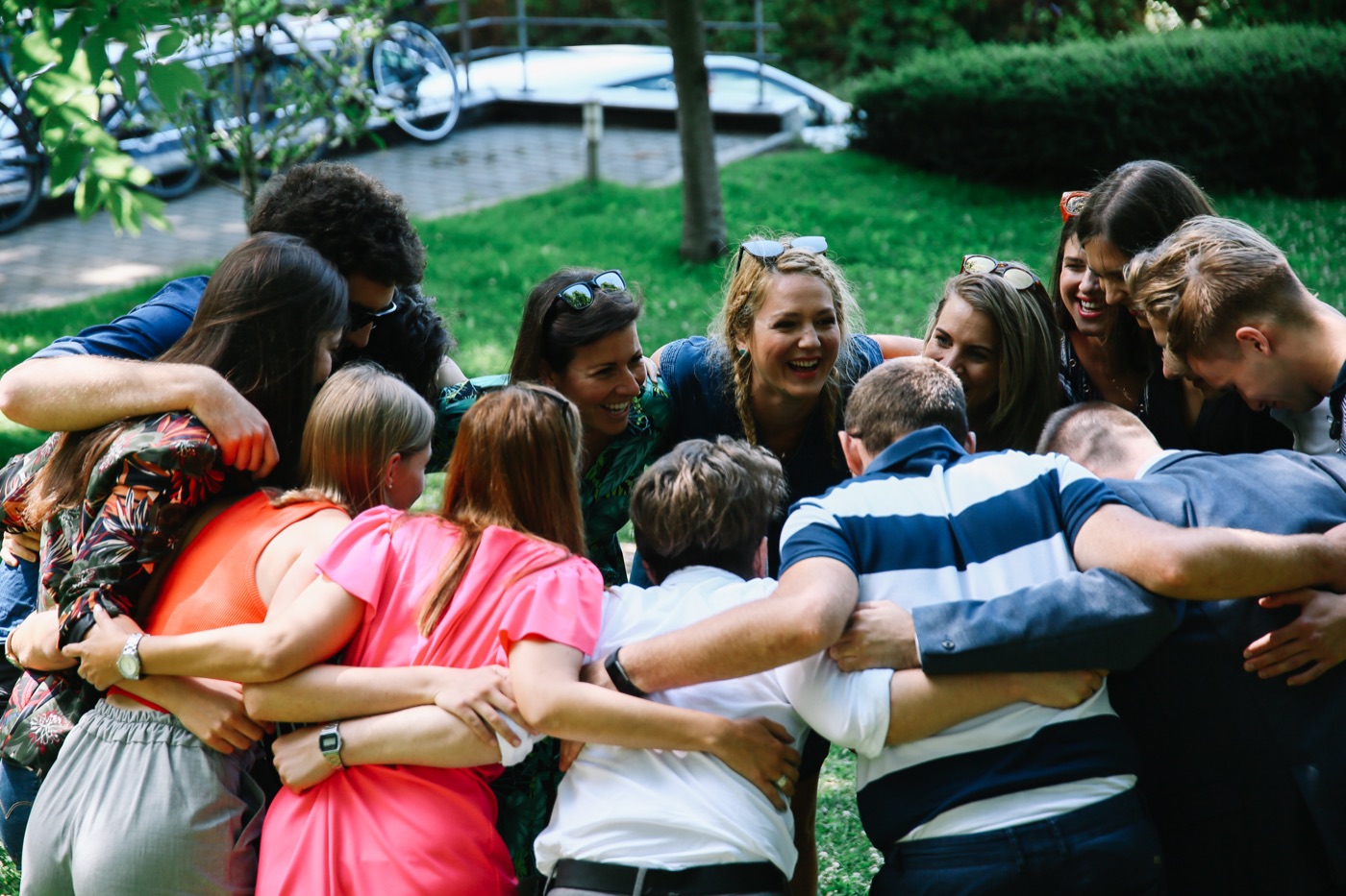 A group standing in a close circle, arms around each other, laughing together